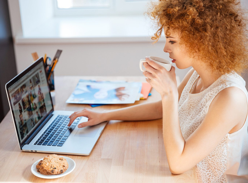 Woman photographer drinking coffee and working with laptop on workplace